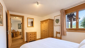 A bedroom with a large bed, wooden wardrobe, a mirror, and a window with a view.