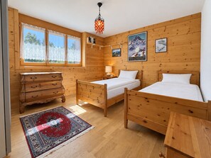 Een kamer met houten wanden, twee eenpersoonsbedden, een dressoir, een tapijt en een hanglamp.