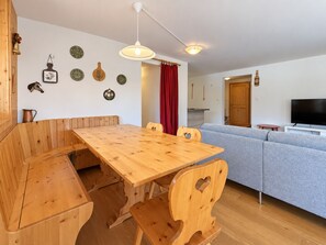 Un coin repas avec une table et des bancs en bois, un canapé, un téléviseur et des éléments décoratifs fixés au mur.