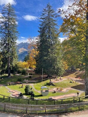 Un parc avec un ciel dégagé, des arbres aux couleurs automnales et une sculpture au centre.