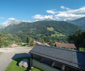 A mountain view with a chalet-style building in the foreground, a paved driveway, and a clear sky.