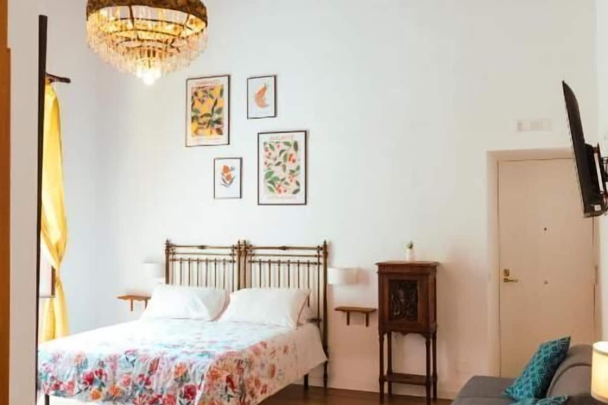 Un dormitorio con techo de madera, una cama con ropa de cama floral, una mesita de noche, un armario pequeño y un televisor en la pared.