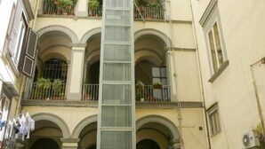 A multi-story building with balconies, a central glass elevator shaft, and a ground-level entrance with a sign. - Relais CuoreNapoletano (Naples)