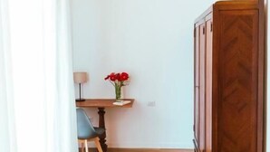 A room with a wooden floor, a desk with a lamp, a chair, a cabinet, and a vase with red flowers. - Relais CuoreNapoletano (Naples)