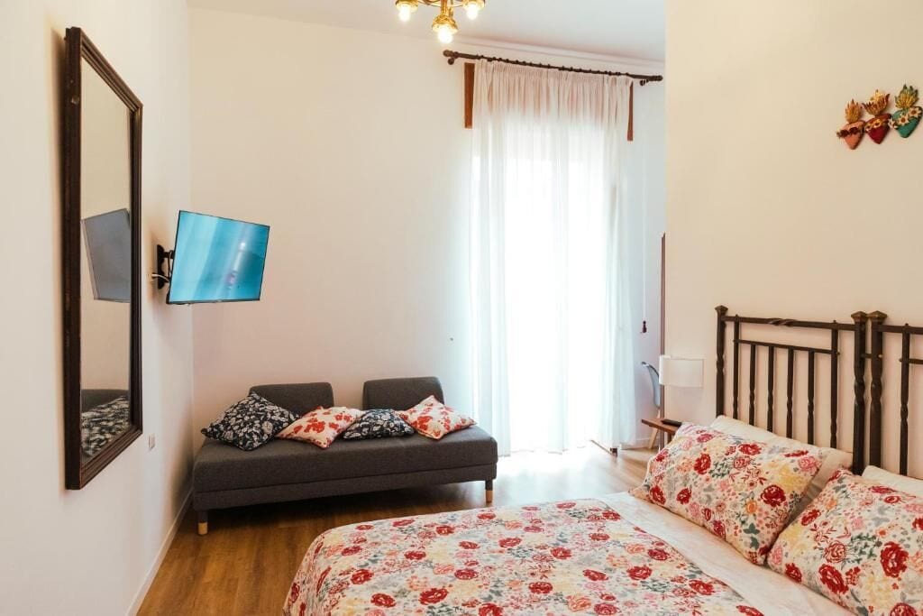 A bedroom with a bed, a sofa, a TV, and a window with curtains.