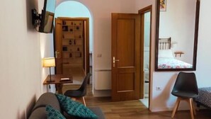 A compact living space with a sofa, a dining table, a chair, a mirror, and a chandelier. - Relais CuoreNapoletano (Naples)