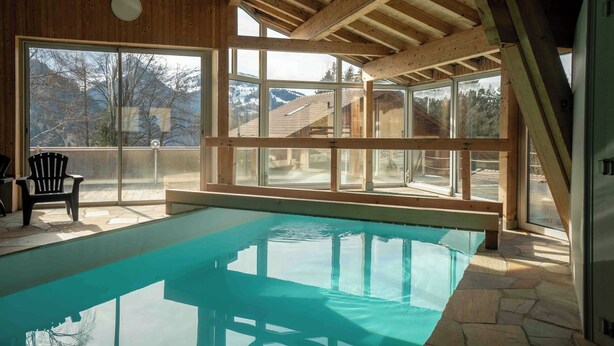Piscina con techo de madera y amplios ventanales que ofrecen vistas a la montaña.