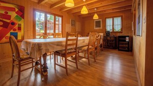 Comedor de madera con una mesa dispuesta para seis, sillas de madera, lámparas colgantes y vistas al exterior a través de ventanas amplias.