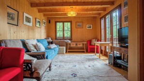 Un interior de cabaña acogedor con paredes de madera, un sofá azul, un sillón rojo, una mesita y un televisor.