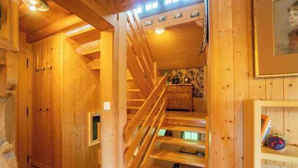 Interior de madera con una escalera, paredes de madera y una pequeña zona de cocina.