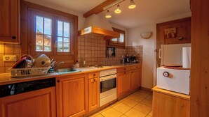 Una cocina con armarios de madera, lavavajillas, horno, refrigerador y ventana con vista a edificios.