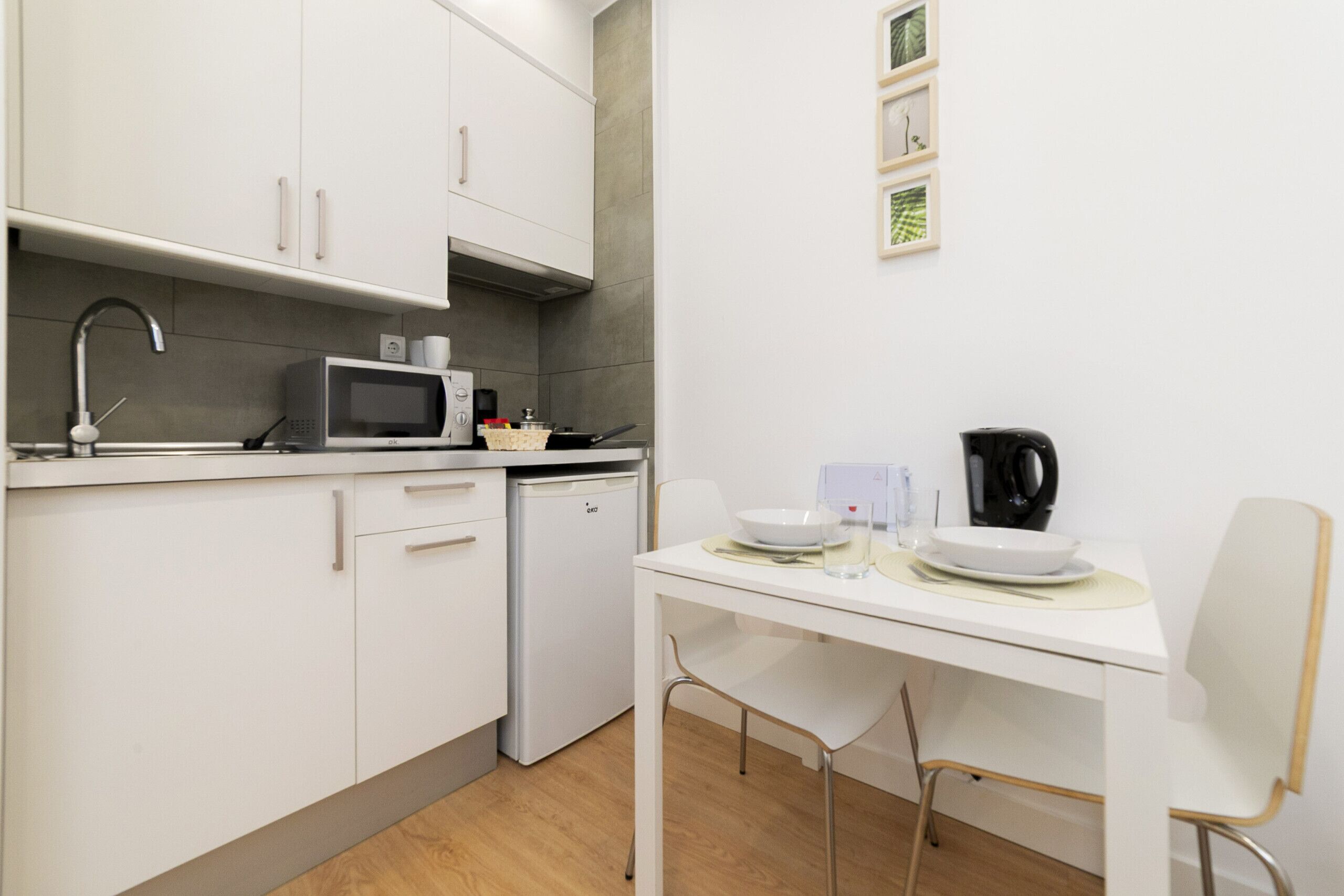 A modern kitchen with white cabinets, a microwave, a coffee maker, and a dining table with chairs.