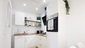 Una cocina moderna con armarios blancos, encimera de madera y horno negro. Se observan estantes con objetos decorativos y una planta colgante.