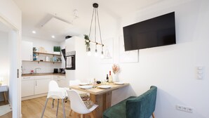 Una cocina moderna con comedor, piso de madera, armarios blancos y un televisor de pantalla plana montado en la pared.