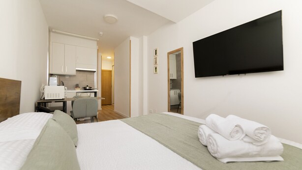 Una habitación de hotel con cama, escritorio, silla, televisor y kitchenette.