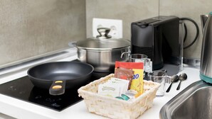 A kitchen with an induction cooktop, a frying pan, a pot, a coffee maker, a basket of tea bags, and a glass of water. - Classy IX - Ferga Suites (Madrid)