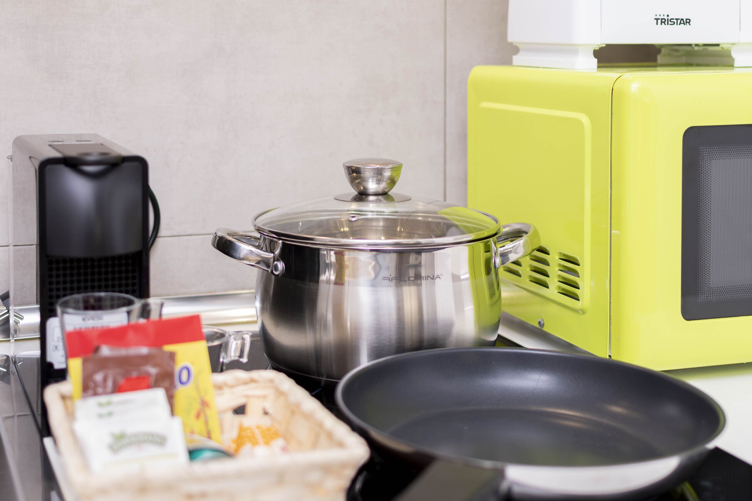 Une cuisine avec une casserole en acier inoxydable sur la cuisinière, une poêle, une machine à café et un appareil électroménager d’un vert vif.