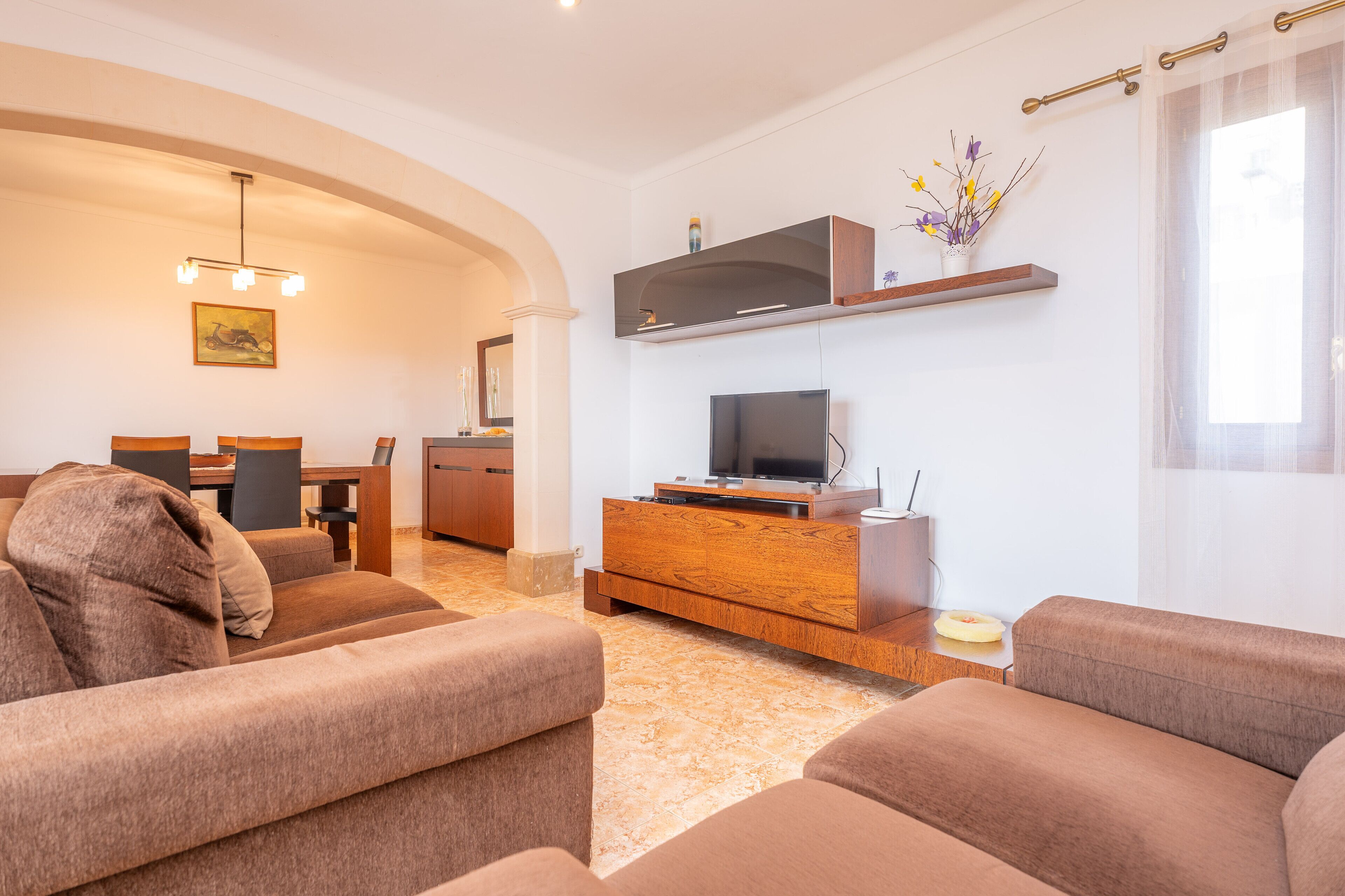Uma sala de estar moderna com um sofá, uma TV sobre um suporte de madeira e uma área de jantar com mesa e cadeiras.