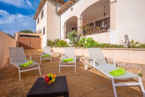 A patio with white lounge chairs and a table with fruit.