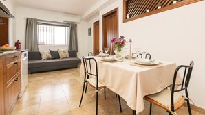 Un coin repas avec une table dressée pour quatre personnes, un canapé et un espace cuisine équipé de placards et d’un évier.