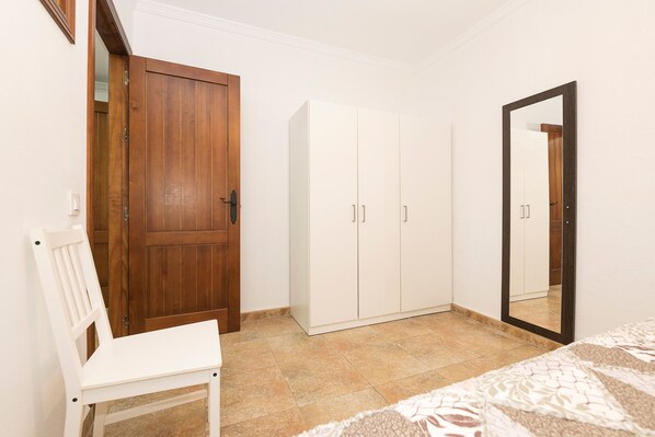 A bedroom with a wooden wardrobe, a white wardrobe, a mirror, and a white chair.