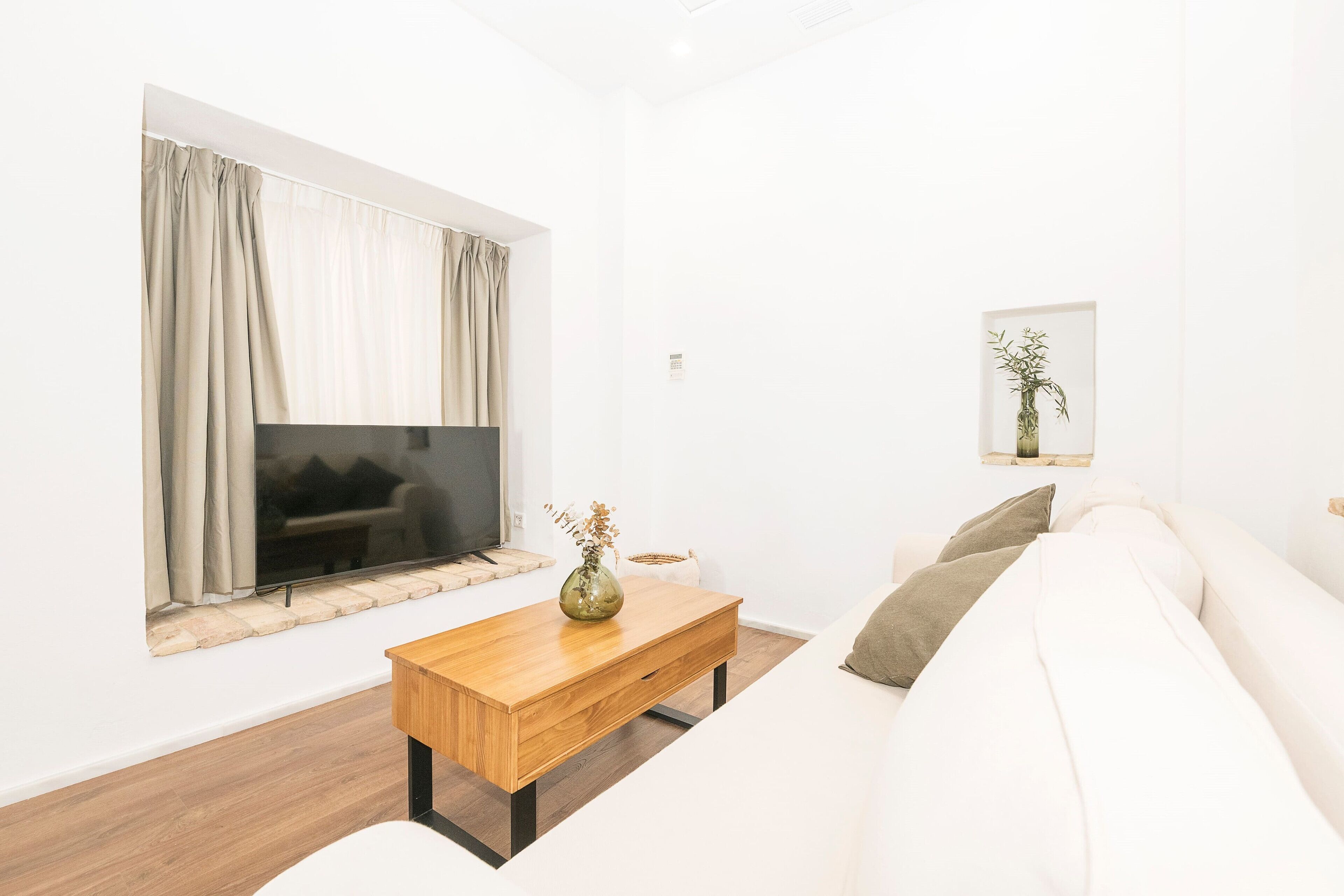 A modern living room with a flat-screen TV, a wooden coffee table, a white sofa, and a framed artwork on the wall.