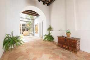 A spacious hallway with terracotta tiles, white walls, and wooden beams. There are potted plants and a wooden chest of drawers. - Mar Abierto A in Sanlucar de Barrameda (Sanlucar de Barrameda)
