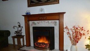 Una chimenea con repisa, un reloj encima y un florero con flores secas a la derecha.