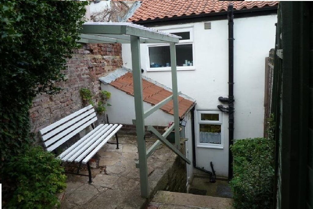 Ein schmaler Außenkorridor mit einer weißen Bank, einer Backsteinmauer und einem Gebäude mit einem Ziegeldach.