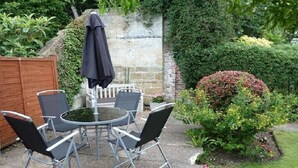 Un patio con una mesa redonda y cuatro sillas, una sombrilla negra y una valla de madera.