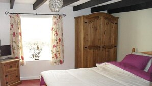 Un dormitorio con cama, armario de madera, cómoda y ventana con cortinas florales.