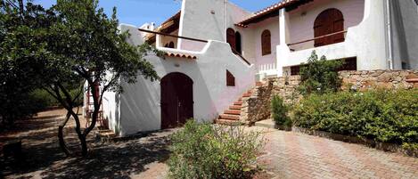 Un edificio tradicional blanco con techo de tejas rojas, una escalera de piedra y un patio empedrado.