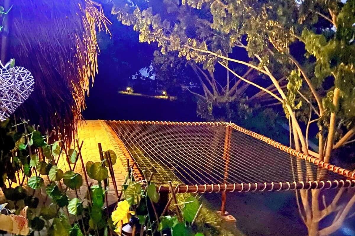 Una construcción con techo de paja, una hamaca y un área protegida por mosquitero, rodeada de vegetación.
