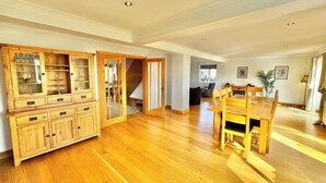 Amplia sala de estar con piso de madera, una mesa de comedor y un mueble empotrado de madera con puertas de vidrio.
