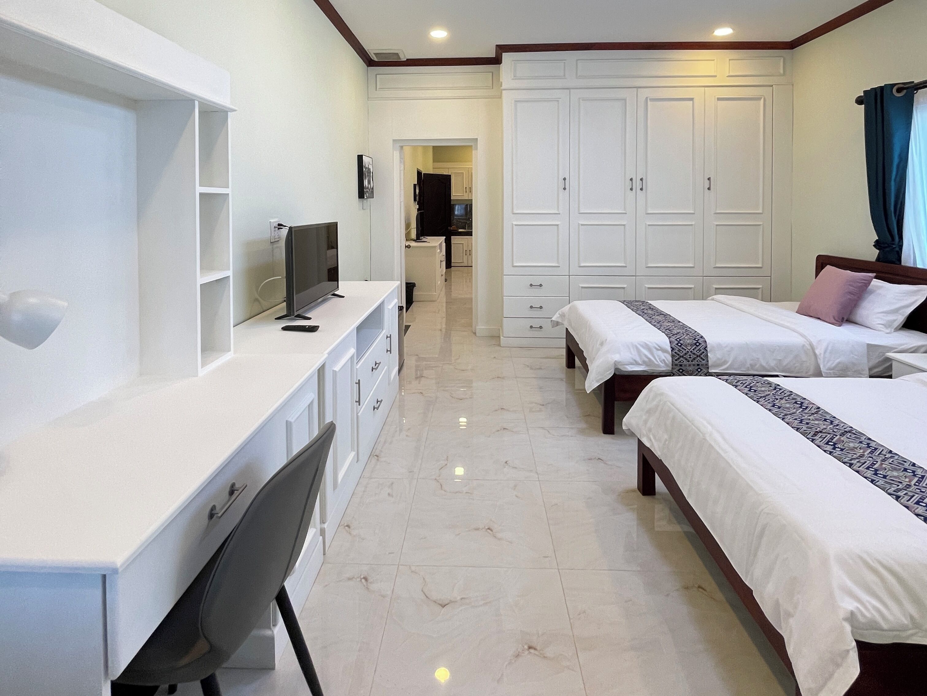 A hotel room with a desk, two beds, a TV, and a wardrobe.