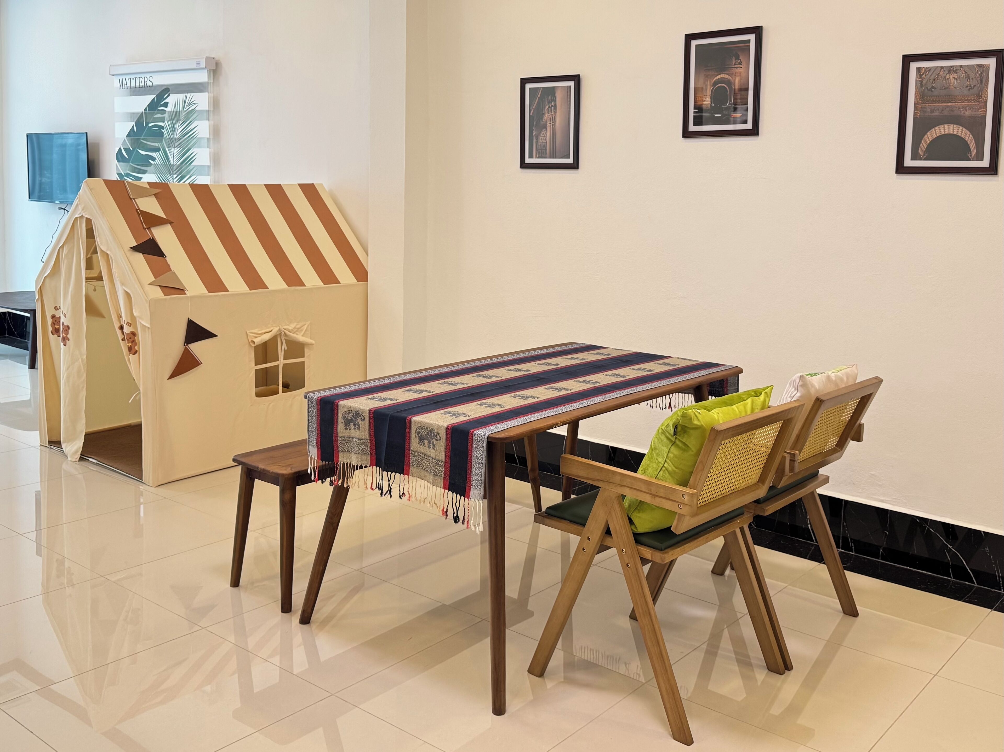 Una casita de juegos con techo a rayas, una mesa con mantel estampado y dos sillas con cojines.