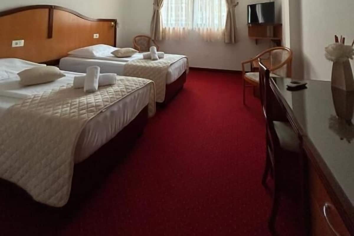 A hotel room with two beds, a desk, a chair, a TV, and a window with curtains.