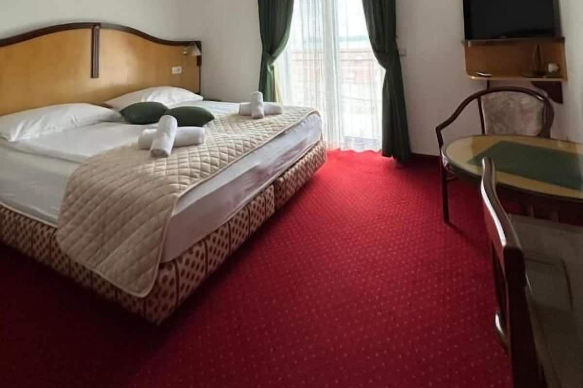 A hotel room with a bed, a desk, a chair, a TV, and an air conditioning unit.
