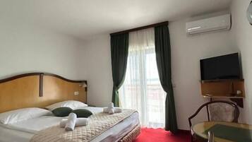 Una habitación de hotel con cama, escritorio, silla, televisor y aire acondicionado.