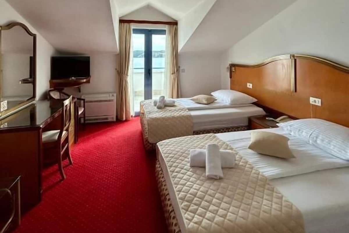 A hotel room with two beds, a desk, a television, and a large window.