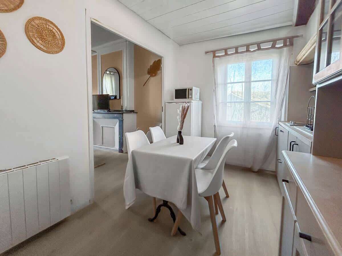 Een kamer met een eettafel, stoelen, een keukenhoek en een raam met gordijnen.