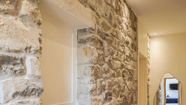 A stone wall with a built-in shelf, a mirror, and a hallway leading to another room.