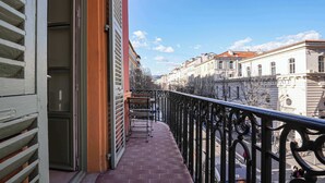 A balcony with a view of a city street, a building with 'Generale' on it, and a clear sky.