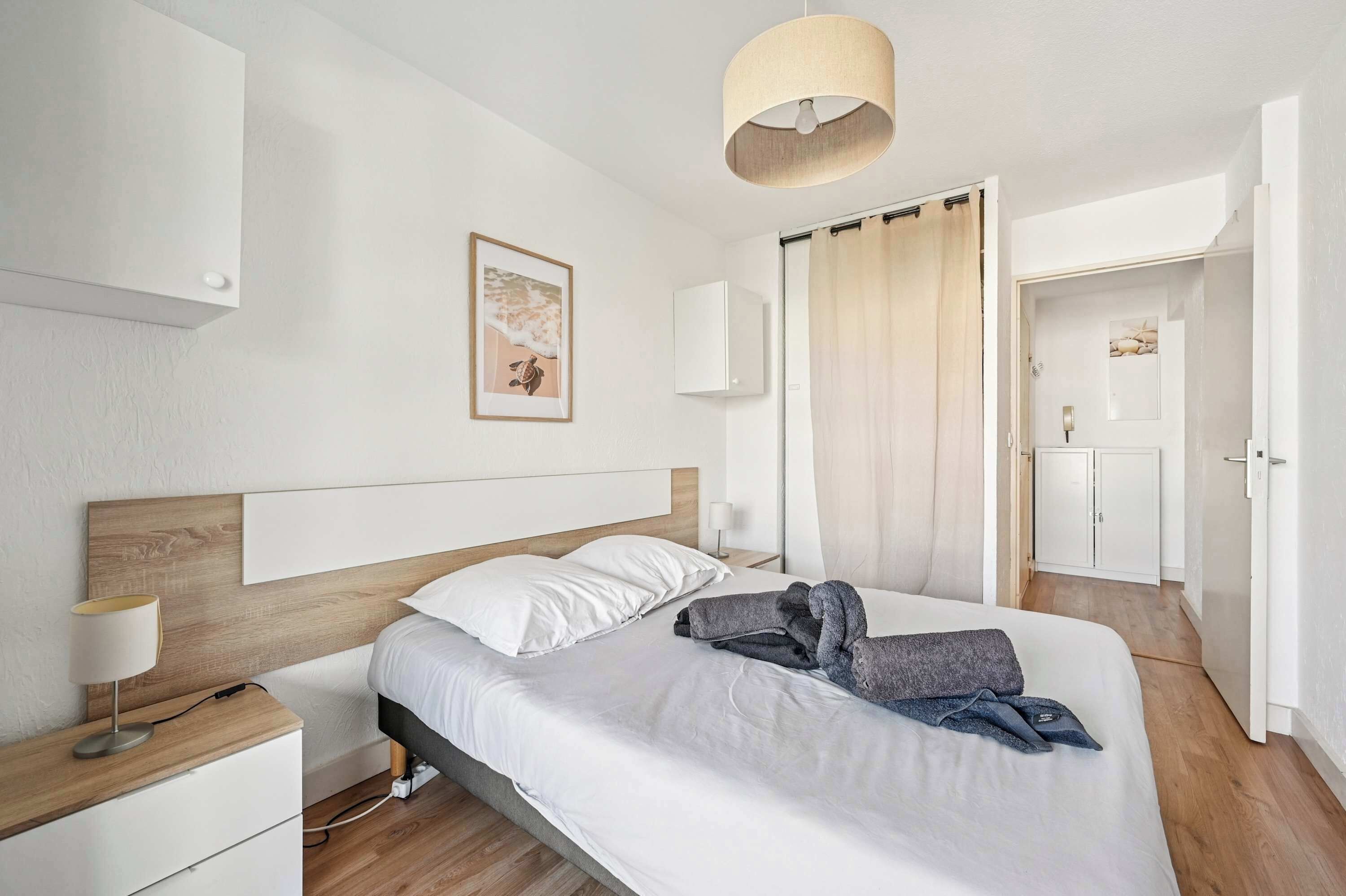 A modern bedroom with a wooden headboard, a single bed with white linens, a bedside table with a lamp, and a wardrobe.