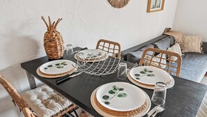A dining table set with plates, glasses, and cutlery, surrounded by wicker chairs and a woven placemat. - Le Cap Vert - 4 pers, terrasse & piscine (Mandelieu-la-Napoule)