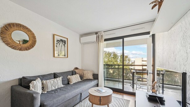 A modern living room with a grey sofa, a round wooden coffee table, a large mirror, and a framed picture on the wall. - Le Cap Vert - 4 pers, terrasse & piscine (Mandelieu-la-Napoule)