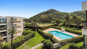 A modern building with a pool surrounded by well-maintained gardens and a mountain in the background. - Le Cap Vert - 4 pers, terrasse & piscine (Mandelieu-la-Napoule)