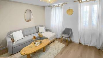A living room with a sofa, a coffee table, a chair, a hanging light fixture, and a wall-mounted mirror.