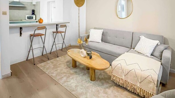 A modern living room with a grey sofa, a wooden coffee table, and a dining area with a white countertop and bar stools. - Le Petit Rempart, T2 vue sur remparts de la Cité (Carcassonne)