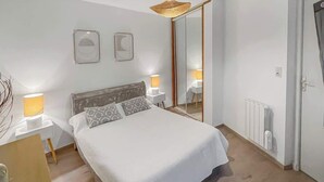 A bedroom with a bed, bedside lamps, a mirror, and a radiator. - Le Petit Rempart, T2 vue sur remparts de la Cité (Carcassonne)